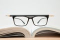 Glasses, open book, pencil on wooden table, white background and copy space