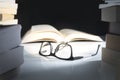 Glasses and open book on table surrounded by literature. Royalty Free Stock Photo