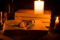 Glasses on the open book under the burning candle lights Royalty Free Stock Photo