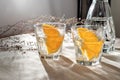 Glasses with orange infused water and bottle on beige table with aesthetic sunlight shadows, lifestyle healthy drink, alcohol Royalty Free Stock Photo