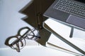 Glasses and a part of a laptop on white file folders with harsh shadows on an office desk, business work concept, copy space, Royalty Free Stock Photo