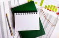 Glasses, a pen and a green diary with a business card lie on the desktop against the background of reports and charts. Close-up of Royalty Free Stock Photo