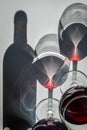 Glasses of red wine and bottle with shadows and reflections on a white textured surface. Royalty Free Stock Photo