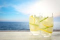 Glasses of refreshing lemonade on table near sea, space for text