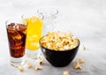 Glasses of soda drink with ice cubes and black bowl of popcorn snack on stone kitchen table background. Cola and orange and clear Royalty Free Stock Photo