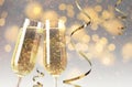 Glasses with sparkling wine and shiny serpentine streamers against blurred festive lights Royalty Free Stock Photo