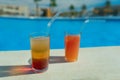 Glasses with tasty cocktail in front of a swimming pool with clear water. Close-up photo. Palm trees on the background. Vacation a
