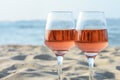 Glasses of tasty rose wine on sand near sea, closeup. Space for text Royalty Free Stock Photo