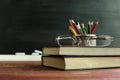 Glasses teacher books and a stand with pencils on the table, on the background of a blackboard with chalk. The concept of the teac Royalty Free Stock Photo