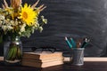 Glasses teacher books and wildflowers bouquet on the table, on background blackboard with chalk. The concept of the teacher`s day