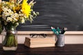 Glasses teacher books and wildflowers bouquet on the table, on background blackboard with chalk. The concept of the teacher`s day