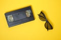 glasses for watching 3D movies and videotape on pink and yellow background, vintage video cassette copy space