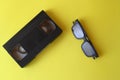 Glasses for watching 3D movies and videotape on yellow background, vintage video cassette copy space