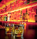 Glasses of whiskey with ice on bar table near whiskey bottle on warm atmosphere