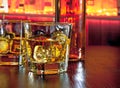 Glasses of whiskey with ice on bar table near whiskey bottle on warm atmosphere