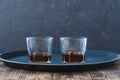 Glasses of whiskey with ice cubes on a black tray and wooden table/Two Glasses of whiskey with ice cubes on a black tray and Royalty Free Stock Photo