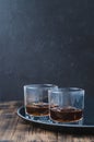 Glasses of whiskey with ice cubes on a black tray and wooden table/Two Glasses of whiskey with ice cubes on a black tray and Royalty Free Stock Photo