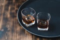 Glasses of whiskey with ice cubes on a black tray and wooden table/Two Glasses of whiskey with ice cubes on a black tray and Royalty Free Stock Photo