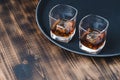 Glasses of whiskey with ice cubes on a black tray and wooden table/Two Glasses of whiskey with ice cubes on a black tray and Royalty Free Stock Photo