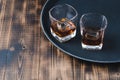 Glasses of whiskey with ice cubes on a black tray and wooden table/Two Glasses of whiskey with ice cubes on a black tray and Royalty Free Stock Photo