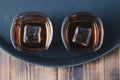 Glasses of whiskey with ice cubes on a black tray and wooden table/Two Glasses of whiskey with ice cubes on a black tray and Royalty Free Stock Photo