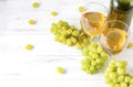 Glasses of white wine, bottle, bunch of green grapes on a white wooden