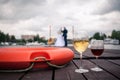 The glasses of wine on the pier next to a life buoy on a background of newlyweds