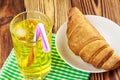 Glassful of lemon soda with ice and tubule on green napkin. croissant, wooden table.