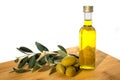 Glassy bottle of olive oil with group of green shiny olives and brunches with leafs