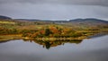 Glassy water reflects the fall red and green scottish landscape as seen from the Calmac Ferry near Kennacraig