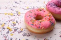 Glazed donuts decorated with sprinkles on white wooden table, closeup. Space for text. Tasty confectionery