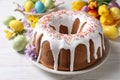 Glazed Easter cake with sprinkles, painted eggs and flowers on white wooden table, closeup Royalty Free Stock Photo