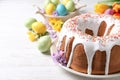 Glazed Easter cake with sprinkles, painted eggs and flowers on white wooden table. Space for text Royalty Free Stock Photo