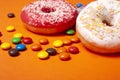 Glazed red and white round bun donuts and multi-colored sweets on orange background. children snacks