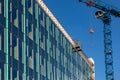Glazed ventilated facade of commercial building and construction crane against blue sky. Fragment of residential building, hotel,