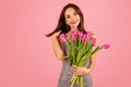 Gleeful young woman with lustrous hair, holding a lush bouquet of pink tulips