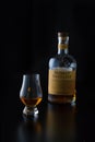 A glencairn glass of whisky is accompanied by a bigger bottle of scotch