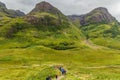 GLENCOE, SCOTLAND - AUGUST 16 2023 - Hikers in the green, dramatic valley of Glen Coe under a moody grey sky