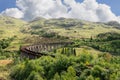 Stone arches of Glenfinnan Viaduct curve amid rugged terrain, under tapestry of undulating hills Royalty Free Stock Photo