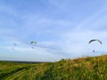 Gliding parachutes flying in blue sky above green hill with grass and path