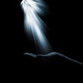 A glimmer of hope flowing down to the hand of the woman on a dark background. The light of faith. Royalty Free Stock Photo