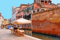 Glimpse of Venice with one of its canals with boats, historic buildings and people drink and relax in outdoor table and chairs of