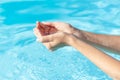 Glitter aquamarine nail polish manicure. Female hands hold water in a palms on a blue pool background