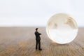 Global and Business Concept. Businessman miniature people figure standing and looking to mini world glass ball on wooden table Royalty Free Stock Photo