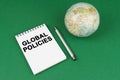 On a green surface lies a model of the planet and a notepad with the inscription - Global Policies