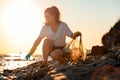 Global environmental pollution. A female volunteer sitting collects plastic bottles on the ocean shore. Cleaning of the Royalty Free Stock Photo