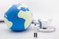 Global Health Care Concept. Close up of doctor miniature figure stanind with patient chart with mini world ball and Stethoscope