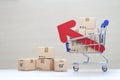 Global inflation or Deflation concept, Red arrow graph and brown parcel box on model miniature shopping cart on wooder background,