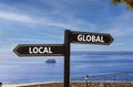 Global or local symbol. Concept word Global or Local on beautiful signpost with two arrows. Beautiful blue sea sky with clouds Royalty Free Stock Photo