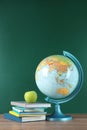 Globe, books and apple on wooden table near green chalkboard. Geography lesson Royalty Free Stock Photo
